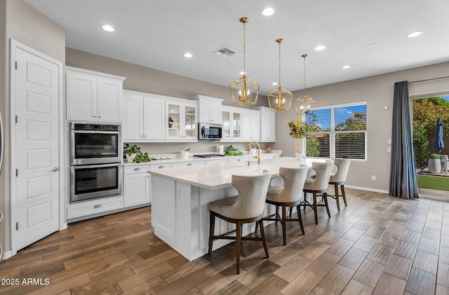 kitchen with a kitchen breakfast bar, light countertops, double oven, a notable chandelier, and an island with sink