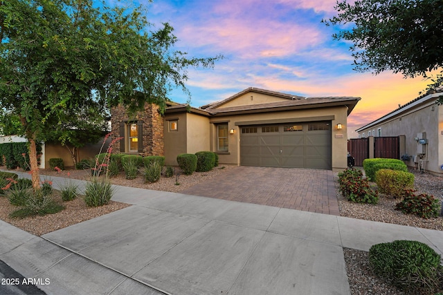 ranch-style home with a garage, decorative driveway, stucco siding, and fence