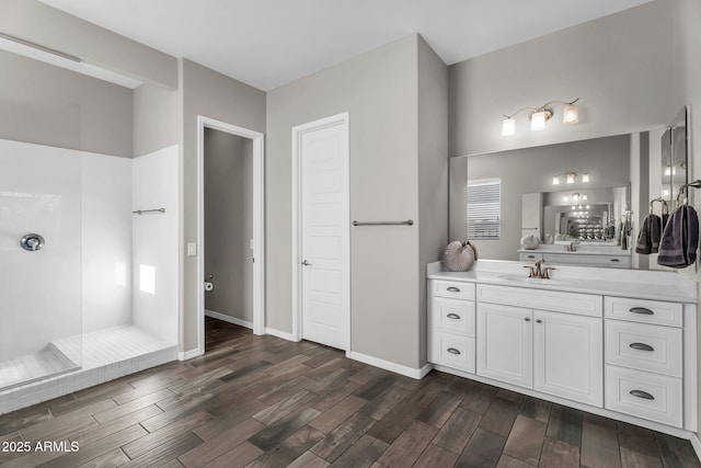 bathroom featuring vanity, baseboards, wood finished floors, and tiled shower