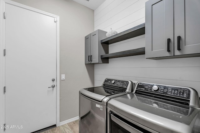 laundry area with cabinet space, light wood finished floors, wood walls, baseboards, and washer and clothes dryer