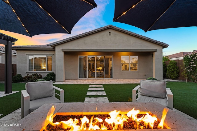 back of property featuring a lawn, stucco siding, a fire pit, and a patio area