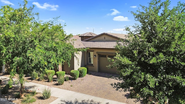 view of front of house with a tiled roof, decorative driveway, an attached garage, and stucco siding