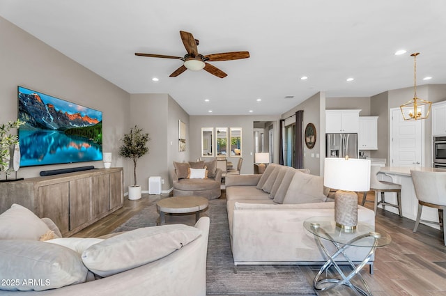 living area featuring recessed lighting, baseboards, ceiling fan with notable chandelier, and wood finished floors