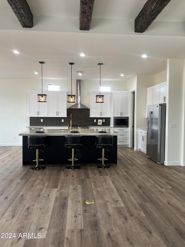 kitchen featuring high quality fridge, wall chimney exhaust hood, decorative light fixtures, and hardwood / wood-style flooring