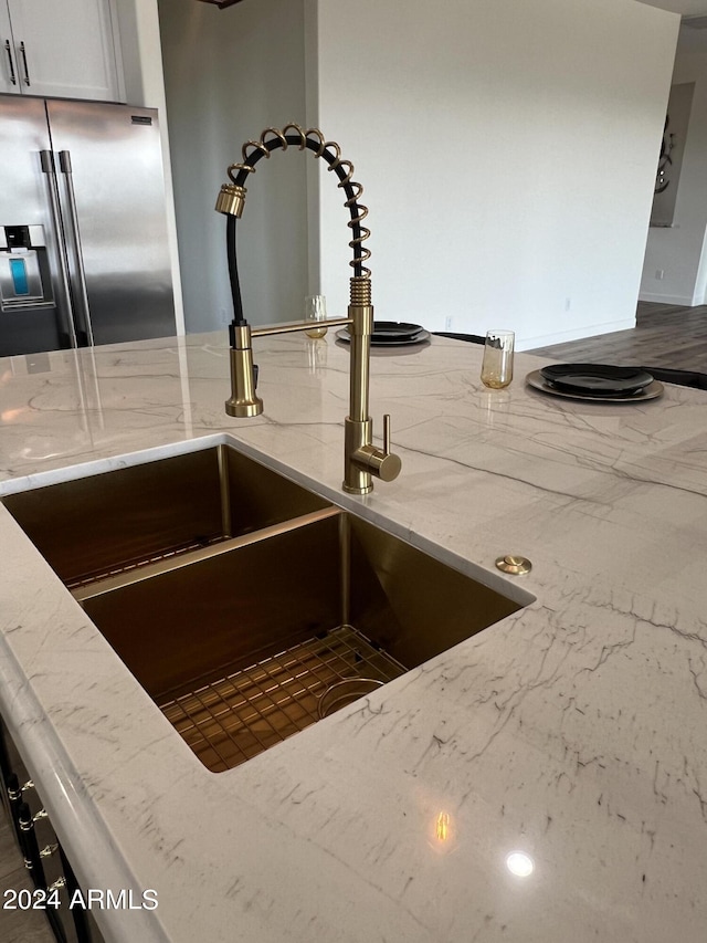 room details with white cabinets, light stone counters, high quality fridge, and sink