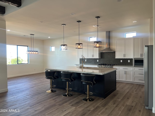 kitchen featuring white cabinets, ventilation hood, a kitchen island with sink, and a healthy amount of sunlight