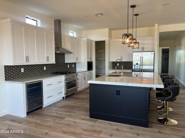 kitchen featuring stainless steel appliances, a kitchen island with sink, sink, wall chimney range hood, and wine cooler