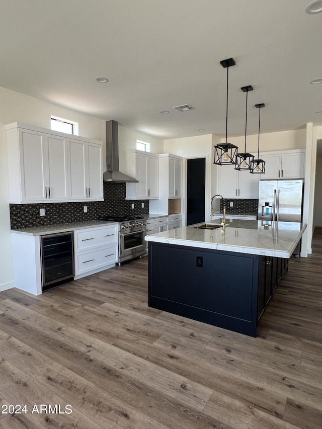 kitchen with sink, wall chimney exhaust hood, wine cooler, pendant lighting, and appliances with stainless steel finishes