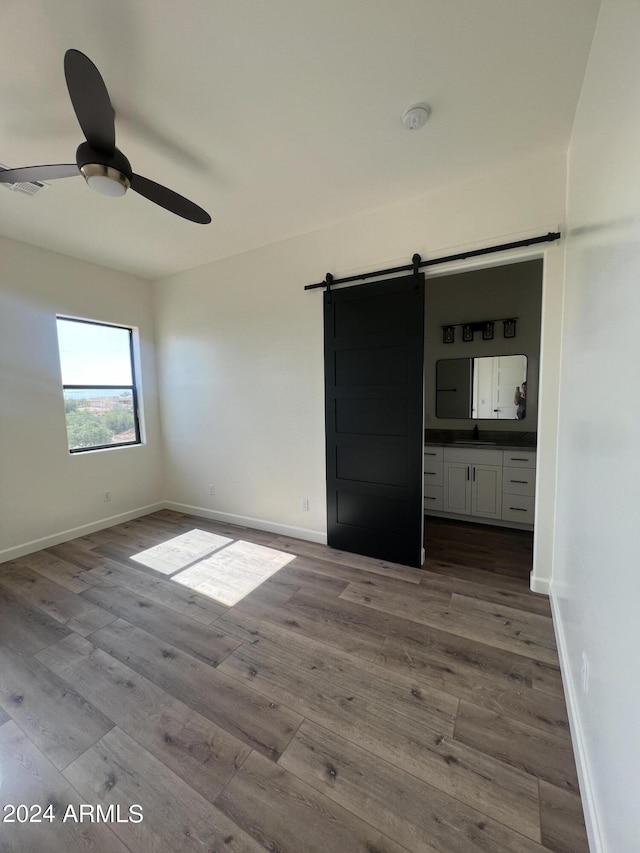 unfurnished room with a barn door, hardwood / wood-style flooring, and ceiling fan