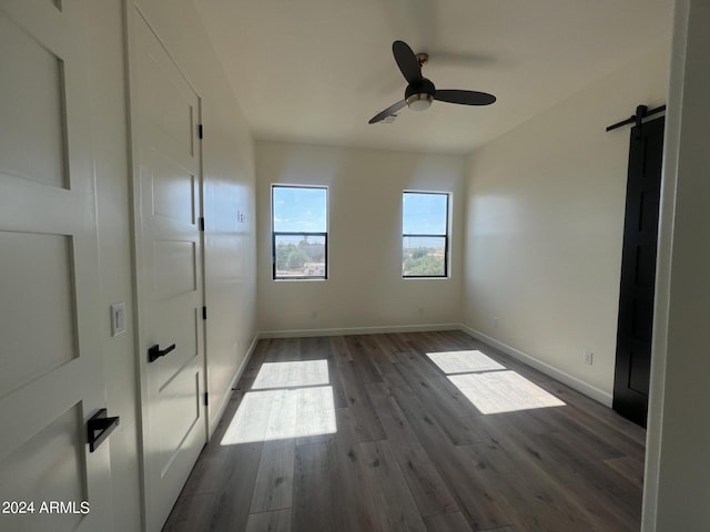 unfurnished bedroom with dark hardwood / wood-style floors, a barn door, and ceiling fan