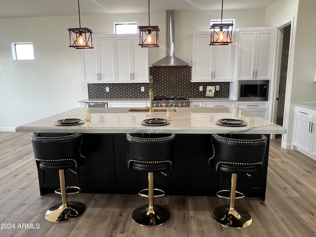 kitchen featuring a breakfast bar area, light stone counters, a center island with sink, and wall chimney exhaust hood