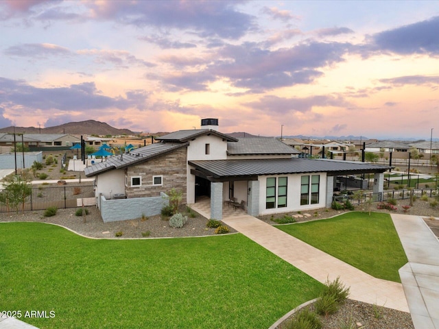 view of front facade with metal roof, stone siding, a lawn, and fence