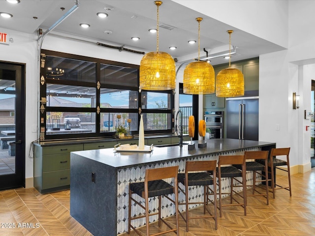 kitchen with dark countertops, green cabinets, a kitchen bar, high end refrigerator, and a sink