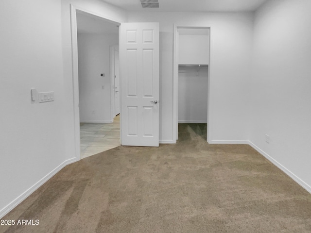 unfurnished bedroom featuring carpet flooring, visible vents, a walk in closet, and baseboards