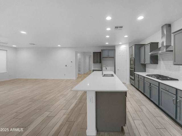 kitchen featuring visible vents, wood finish floors, wall chimney range hood, appliances with stainless steel finishes, and a sink