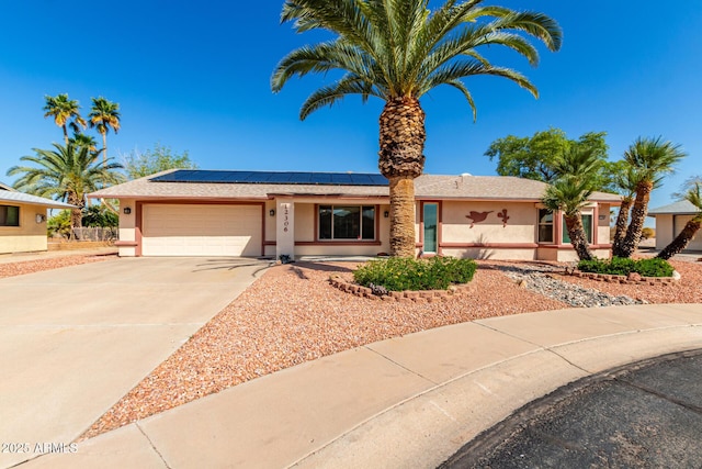 ranch-style home with concrete driveway, an attached garage, roof mounted solar panels, and stucco siding