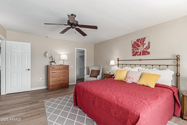 bedroom with wood finished floors, baseboards, a ceiling fan, a closet, and a walk in closet