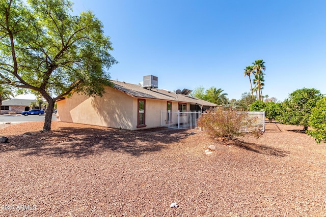 rear view of property featuring stucco siding, central air condition unit, and fence