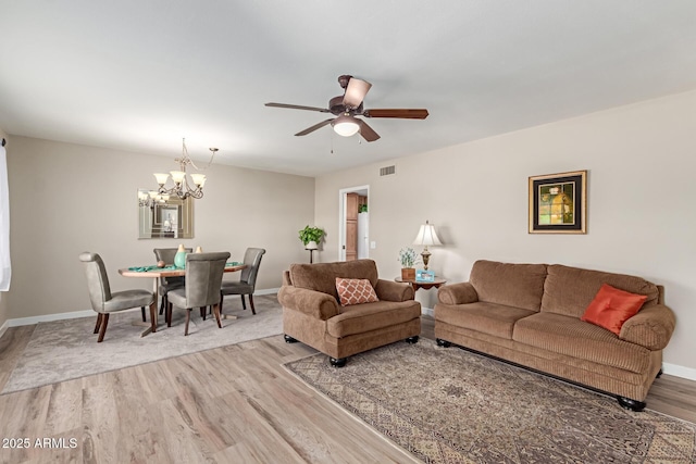 living area with ceiling fan with notable chandelier, light wood-style flooring, baseboards, and visible vents