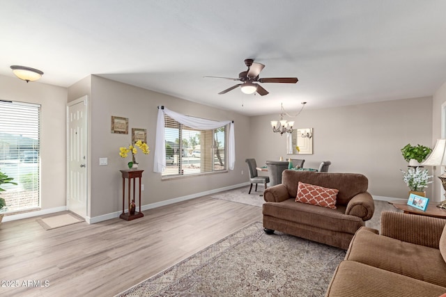 living area with baseboards, light wood-style flooring, and ceiling fan with notable chandelier