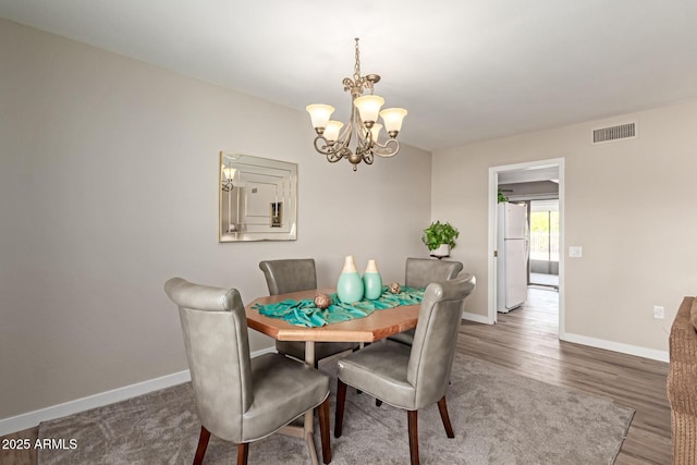 dining space with visible vents, baseboards, wood finished floors, and a chandelier