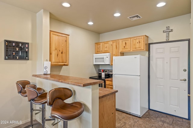 kitchen featuring white appliances, kitchen peninsula, light tile patterned floors, a kitchen breakfast bar, and light brown cabinetry