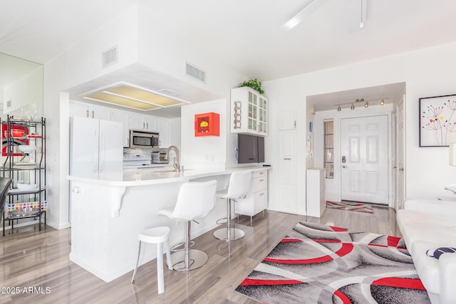 kitchen with white appliances, visible vents, a breakfast bar, a peninsula, and white cabinetry