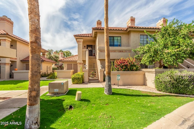 mediterranean / spanish-style house with stairs, a tiled roof, stucco siding, a front lawn, and a chimney