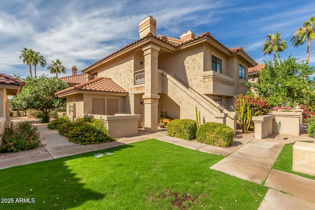 view of front facade with a front yard, a tile roof, a chimney, and stucco siding