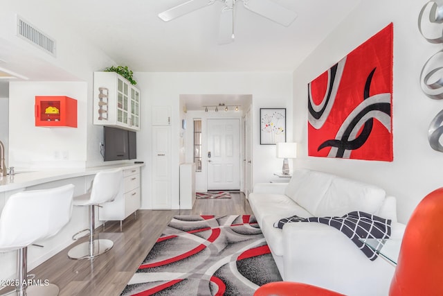 living room with wood finished floors, visible vents, and a ceiling fan