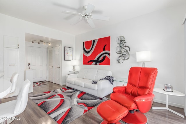 living area with baseboards, track lighting, a ceiling fan, and wood finished floors