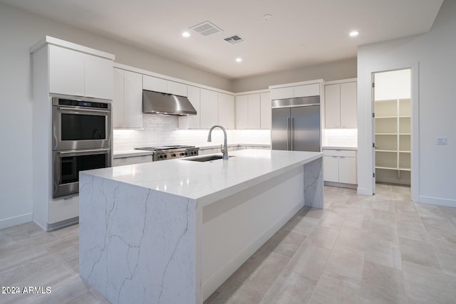 kitchen featuring ventilation hood, light stone countertops, appliances with stainless steel finishes, white cabinets, and a center island with sink