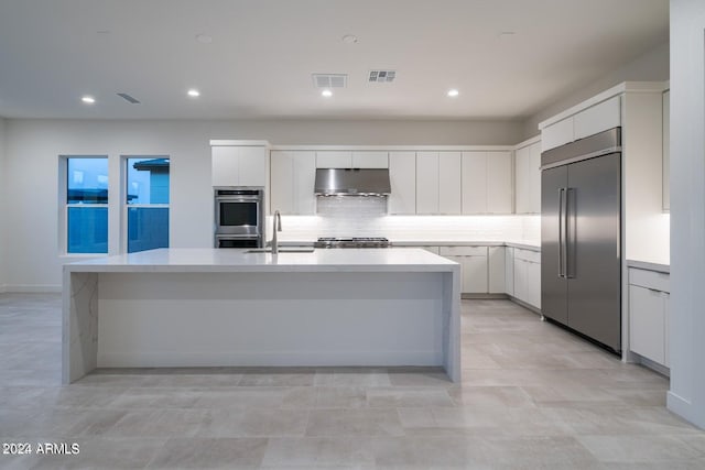 kitchen featuring appliances with stainless steel finishes, sink, white cabinets, decorative backsplash, and a center island with sink