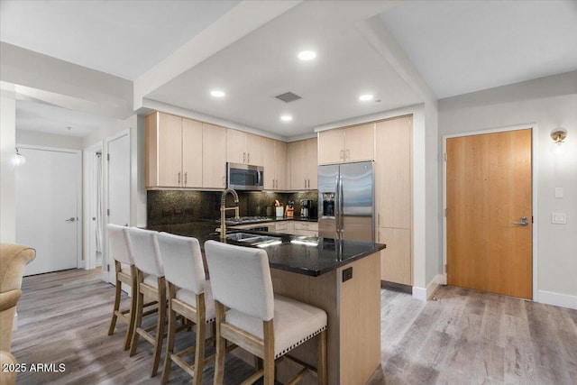 kitchen featuring backsplash, light hardwood / wood-style flooring, light brown cabinets, and appliances with stainless steel finishes