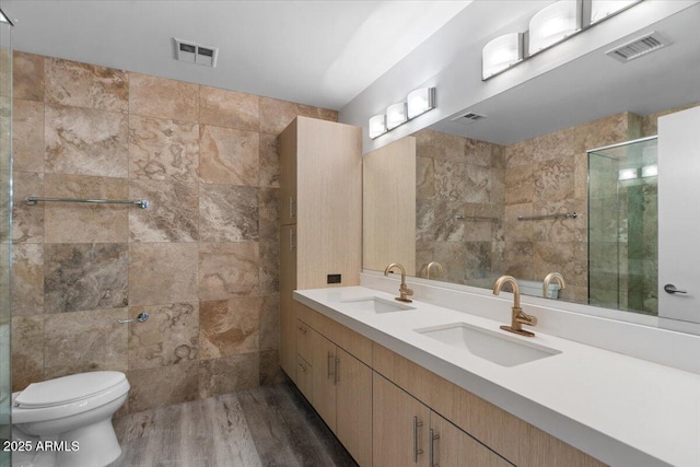 bathroom with tile walls, vanity, wood-type flooring, toilet, and walk in shower