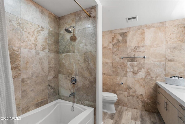 full bathroom with hardwood / wood-style floors, tile walls, tiled shower / bath combo, vanity, and toilet