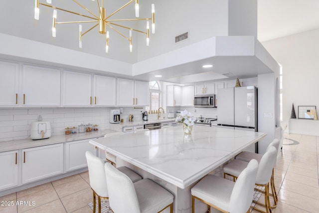 kitchen with pendant lighting, light tile patterned floors, light stone counters, white cabinetry, and stainless steel appliances