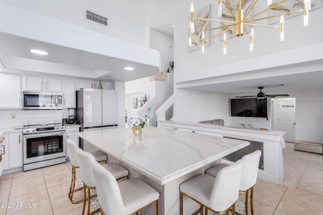 kitchen with white cabinets, appliances with stainless steel finishes, decorative light fixtures, and a breakfast bar area