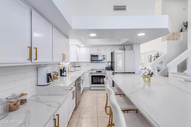 kitchen featuring white cabinets, light stone countertops, a breakfast bar area, and appliances with stainless steel finishes