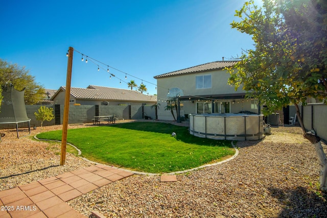 rear view of house featuring a yard, a covered pool, and a trampoline