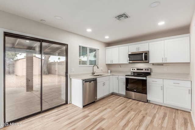 kitchen featuring visible vents, a sink, stainless steel appliances, light countertops, and white cabinetry