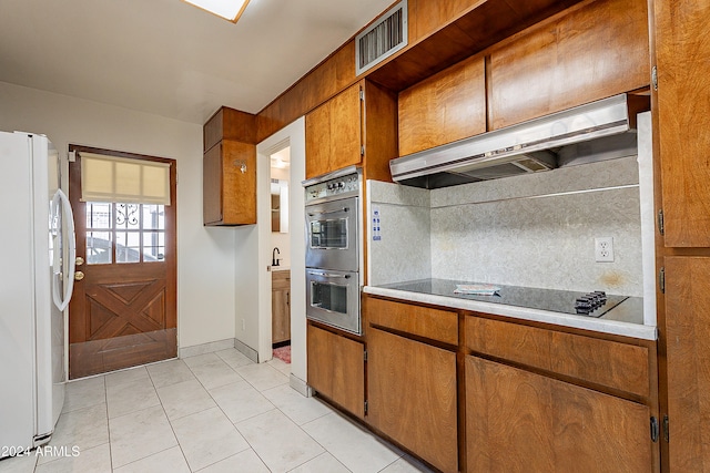 kitchen featuring stainless steel double oven, range hood, white refrigerator, light tile patterned floors, and black electric cooktop