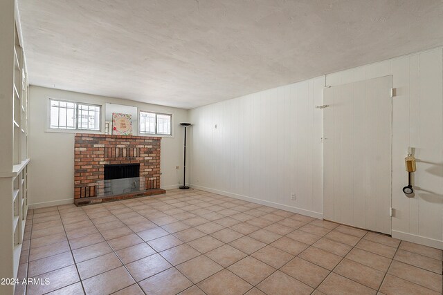 unfurnished living room featuring a brick fireplace and light tile patterned floors