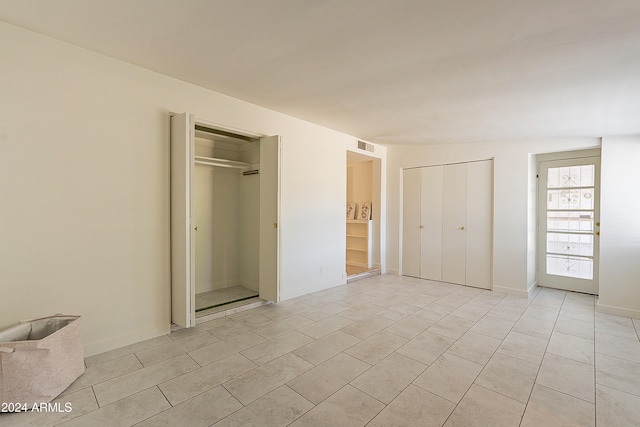 unfurnished bedroom with multiple closets, light tile patterned floors, and vaulted ceiling