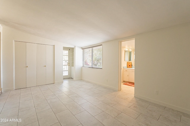 unfurnished bedroom with light tile patterned floors, ensuite bathroom, a closet, and lofted ceiling