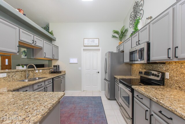 kitchen featuring a sink, stainless steel appliances, decorative backsplash, light tile patterned floors, and light stone counters