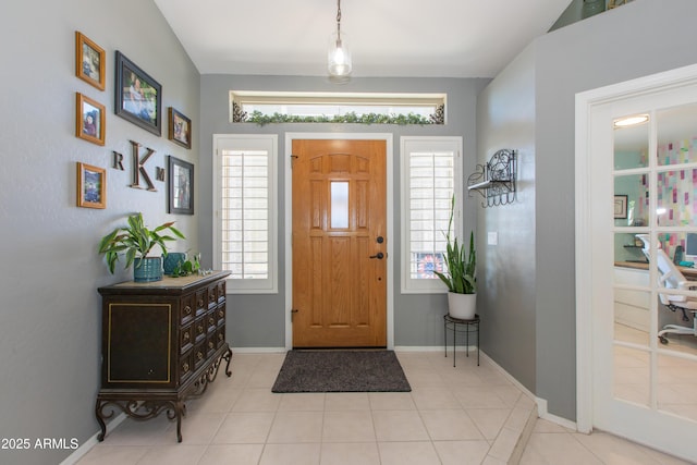 foyer entrance featuring light tile patterned floors, a healthy amount of sunlight, and baseboards