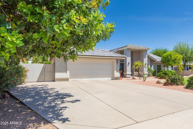 ranch-style home featuring fence, concrete driveway, a tile roof, an attached garage, and stucco siding