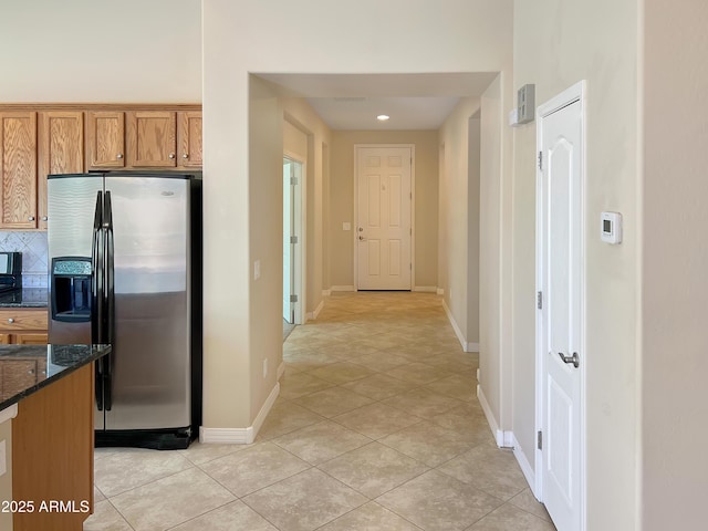 kitchen with light tile patterned floors, backsplash, brown cabinetry, dark stone countertops, and stainless steel fridge