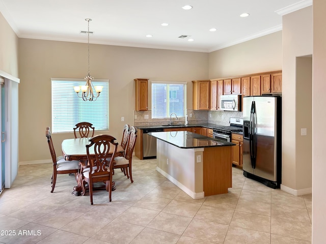kitchen with dark countertops, a kitchen island, ornamental molding, stainless steel appliances, and a sink